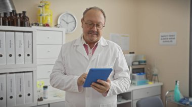 Laboratuvarda beyaz dolaplar ve şişelerle tablet kullanan orta yaşlı bir adam..