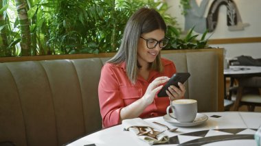Restoranda kahve ve kapalı mekan bitkileriyle akıllı telefon kullanan gülümseyen kadın..