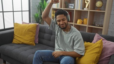Kulaklıklı mutlu adam evde, kanepede müzik dinliyor.