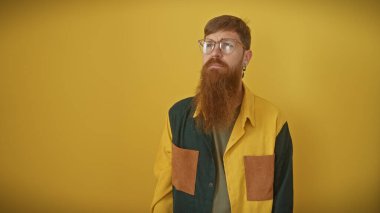Sakallı, gözlüklü, sarı izole bir arka planda poz veren şık bir genç.