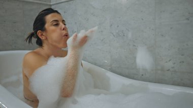Genç bir kadın modern bir banyo ortamında rahatlatıcı köpük banyosunun keyfini çıkarıyor..