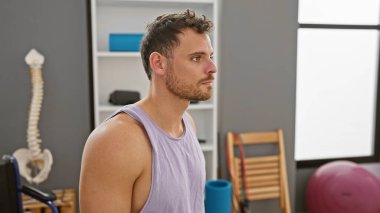 Rehabilitasyon kliniğinde sakallı yakışıklı bir adam, düşünceli bir şekilde başka tarafa bakıyor..