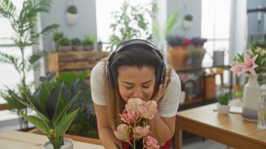 Mutlu bir İspanyol kadın, yeşil ev bitkileriyle çevrili pembe orkide aromasını sever ve müzik dinler..