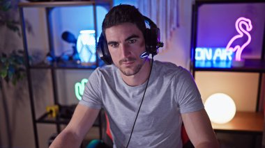 Geceleri karanlık bir oyun odasında kulaklık takan genç İspanyol adam kameraya bakıyor..