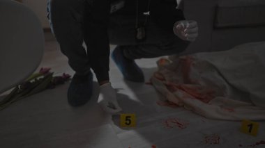 Erkek bir dedektif, kapalı bir suç mahallinde üzerinde numaralandırılmış işaretler, kan ve lalelerle kanıtları inceliyor..