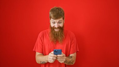 Yakışıklı, kızıl saçlı, mutlulukla dolup taşan, akıllı telefonuna kırmızı izole edilmiş arka plandan mesajlar yazan genç bir adam. Gülüşü ve iyimserliği bulaşıcıdır..