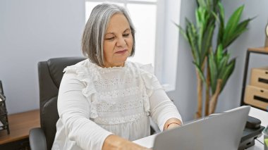 Olgun bir kadın laptopuyla modern ofis ortamında özenle çalışır, profesyonelliği somutlaştırır ve odaklanır..