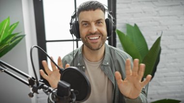 Radyo stüdyosundaki kulaklıklı yakışıklı adam podcast yaparken el kol hareketi yapıyor.