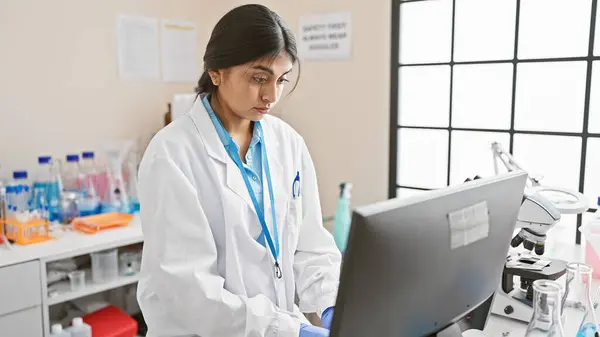 stock image A focused indian woman scientist analyzes data on a computer in a laboratory setting.