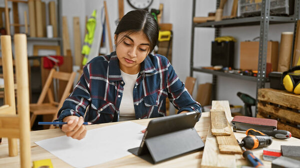 Молодая южно-азиатская женщина рисует в столярной мастерской с инструментами вокруг