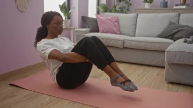 Yetişkin bir Afro-Amerikalı kadın, kıvırcık saçlı kadın evdeki oturma odasında paspasın üstünde spor yapıyor..