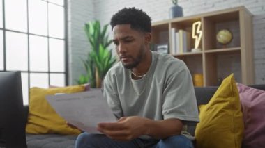 Parlak modern oturma odasındaki telefon ve kapalı salonda bulunan bitkilerle koltukta belgeleri inceleyen odaklanmış bir adam.