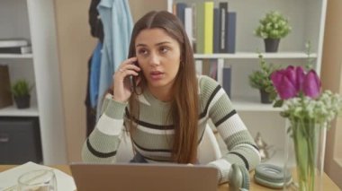 Genç İspanyol kadın ev telefonunda dizüstü bilgisayar ve çiçeklerle sohbet ediyor.