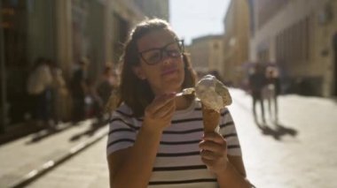 Genç İspanyol bir kadın gözlük takıyor güneşli bir günde güneşli bir caddede dondurma yemekten zevk alıyor. Lecce, puglia, italyan.