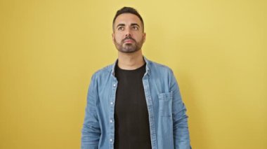 Kotlu gömlekli öfkeli genç bir adam, öfkeyle ayakta duruyor, agresif bir şekilde bağırıyor ve çığlık atıyor. Öfke ve hayal kırıklığı izole edilmiş sarı arka planda..