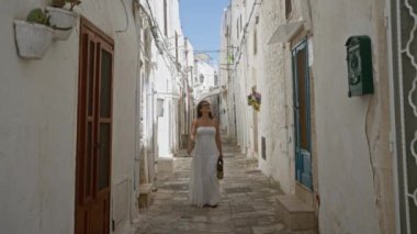 Beyaz elbiseli güzel, genç bir İspanyol kadın Puglia, İtalya 'daki Ostuni kasabasında yürüyor. Açık mavi gökyüzünün altında Avrupa yazının tadını çıkarıyor..