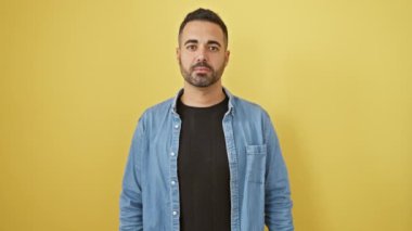 İşkence görmüş, kot gömlek giyen, kör gözlerini eliyle gizleyen, reddedilmeyi simgeleyen genç İspanyol bir adam. İzole edilmiş sarı arkaplan üzerinde dokunaklı bir kesit.