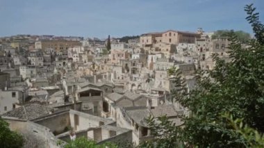 İtalya, Basilicata 'daki antik kasaba materyasının manzarası. Açık mavi gökyüzünün altında yeşillikleri olan tarihi taş binalar sergileniyor..