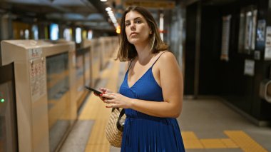 Güzel İspanyol bir kadın, genç bir turist, şehir platformunda metro trenini bekliyor, tren istasyonunda akıllı telefonuyla yazı yazmaya dalmış, tren yolculuğunun bir parçası..