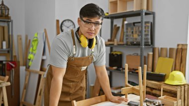 Genç Asyalı bir adam, ahşap ve aletlerle çevrili bir marangozluk atölyesinde dikkatle çalışıyor..