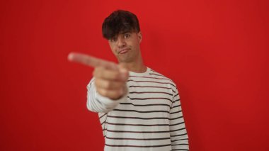 Yakışıklı, İspanyol asıllı, çizgili tişört giyen genç bir adam kamerayı işaret ediyor..