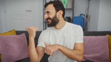 Sakallı adam, modern bir oturma odasını göstererek pozitifliğini ifade ediyor..