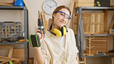 Matkapla kendine güvenen bir kadın, bir marangozluk atölyesinde duruyor, kadınlığın ve zanaatkarlığın bir karışımını sergiliyor..