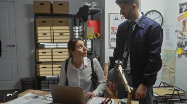 Bir kadın ve bir erkek, muhtemelen dedektifler, dağınık bir polis merkezinde kanıtları inceliyorlar..