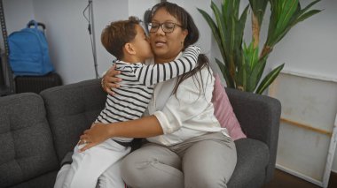 Sevgi dolu bir anne, küçük oğlunu bir oturma odasında rahat bir kanepede kucaklıyor..