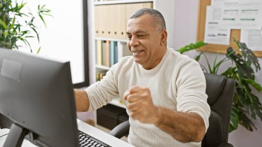 Modern ofiste bilgisayarda çalışan gülümseyen orta yaşlı İspanyol adam.