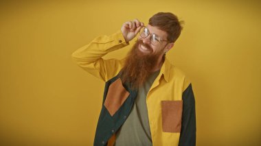 Sarışın, sakallı, gülümseyen ve sarı arka planda gözlük takan yakışıklı bir adam..