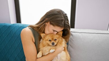 Kendine güveni tam, İspanyol bir kadın evdeki kanepede köpeğiyle samimi bir öpücükten zevk alıyor, neşeli bir gülümseme sergiliyor.