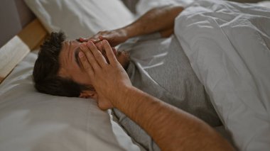 Yatakta uzanmış, elleri kapalı bir yatak odasında yüzünü örten genç bir İspanyol..