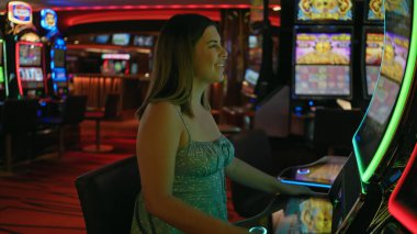 Neşeli bir kumarhanede kumar makinesinde oynayan gülümseyen genç bir kadın..