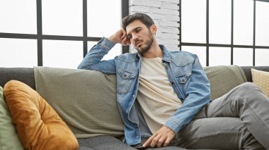 Düşünceli İspanyol bir adam modern bir oturma odasında rahat bir koltukta dinleniyor, sıradan, kentsel yaşam tarzını canlandırıyor..