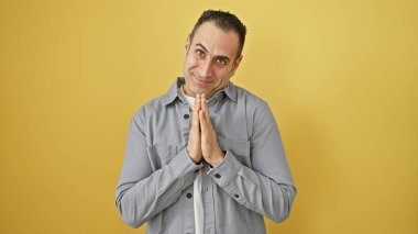 Sarı arka planda duran, gri gömlekli, yalvaran İspanyol bir adam.