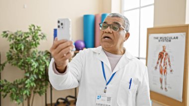 Laboratuvar önlüklü olgun bir adam rehabilitasyon kliniğinde akıllı telefonuyla selfie çeker..