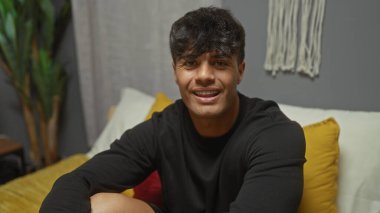 Yakışıklı, genç İspanyol bir adam şık bir yatak odasında bir yatakta otururken gülümsüyor, bunu bir evin içinde günlük veya yaşam tarzı tasviri için mükemmel bir ortam olarak görüyor..