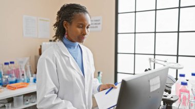 Tıbbi ekipmanlarla çevrili bir laboratuvar ortamında çalışan Afrikalı kadın bilim adamı..