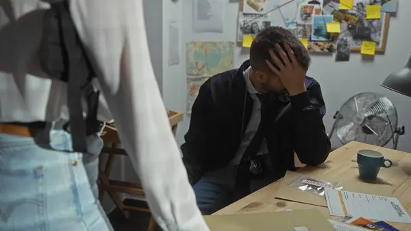 stock image A stressed man and a standing woman in a cluttered investigation office with evidence, including us passports and a board with photos.