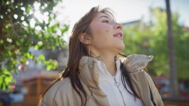 Huzurlu, genç, beyaz bir kadın güneşli bir günün tadını çıkarıyor. Etrafı yeşilliklerle çevrili, huzurlu bir park ortamında..