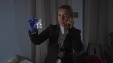 Bir kadın dedektif, kapalı bir suç mahallinde telefon görüşmesi yaparken kanıtları inceliyor..