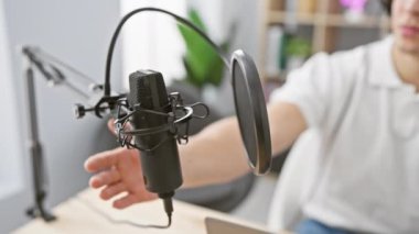 Kapalı bir radyo stüdyosunda mikrofon ayarlayan kıvırcık saçlı İspanyol genç adam podcast kayıt seansını canlandırıyor..
