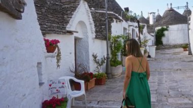 Yeşil elbiseli genç bir İspanyol kadın Puglia, İtalya 'nın büyüleyici tarihi sokaklarını keşfediyor. Geleneksel trulli evler, çiçekler ve beyazlatılmış duvarlarla çevrili..
