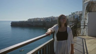 Polignano 'da güneşli bir günün tadını çıkaran genç bir İspanyol kadın. Arka planda çarpıcı bir kıyı şeridi olan kısrak, puglia, İtalya..