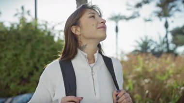 Güneşli bir parkta palmiye ağaçlarıyla barışın tadını çıkaran düşünceli genç bir kadın.