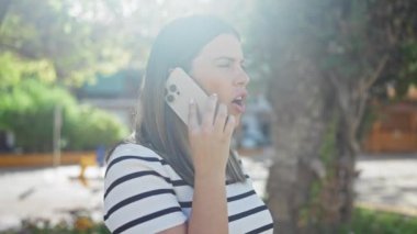 Genç ve çekici bir İspanyol esmer kadın şehir parkının bahçesinde telefonuyla konuşuyor. Şehir yeşilliğinin ortasında dikilirken kaygılarını dile getiriyor ve gözlerine odaklanıyor..