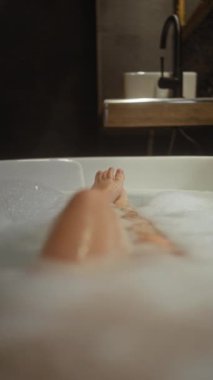 Genç bir kadın modern bir banyoda köpükle rahatlatıcı bir banyonun keyfini çıkarıyor..