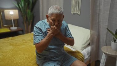 Yatak odasında pijamalı yaşlı İspanyol bir adam. İki eliyle boğazını sıkıyor..