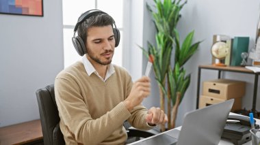 Kulaklıklı yakışıklı İspanyol bir adam ofis ortamında belgeleri analiz ediyor..